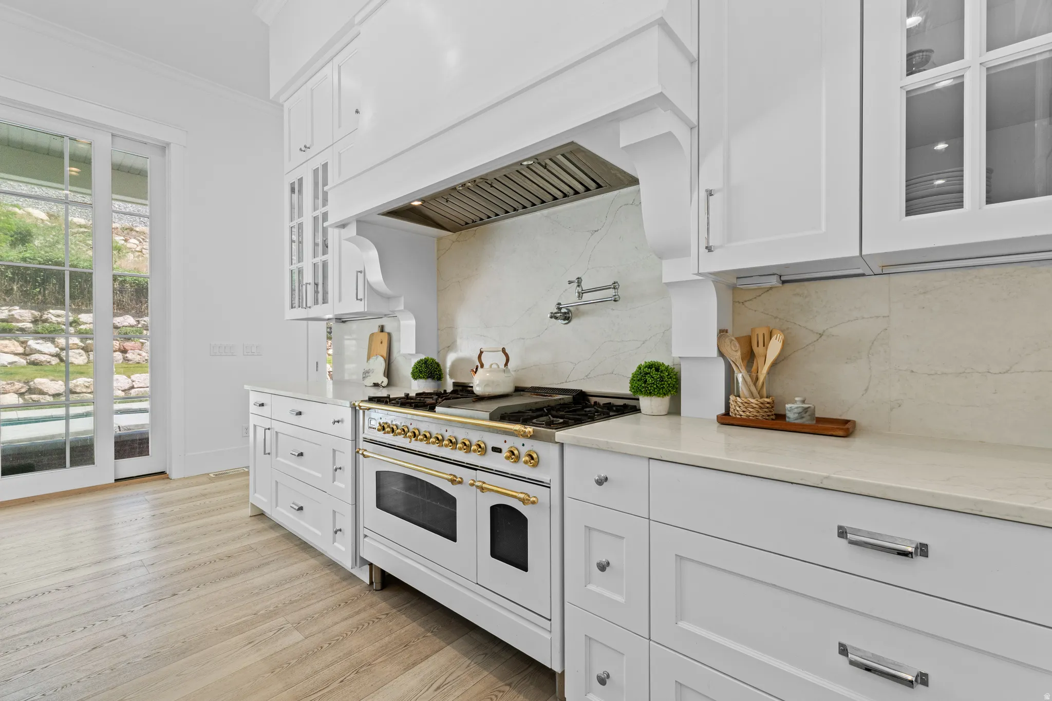Gourmet kitchen featuring a professional-grade range, full-height backsplash, white cabinetry with glass-front accents, and a pot filler
