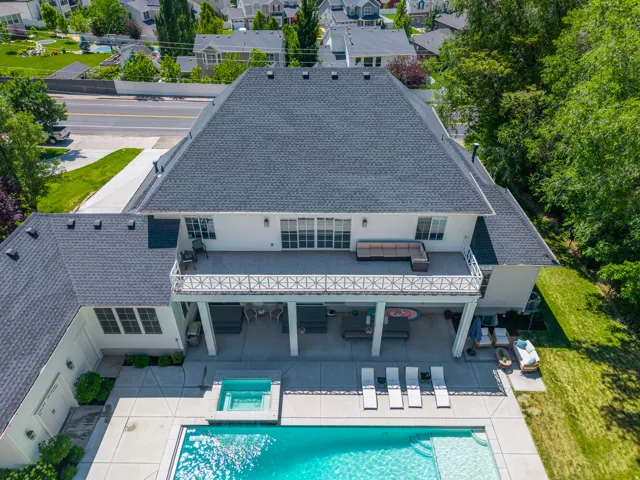 Expansive rear exterior featuring a substantial patio, integrated swimming pool with spa, covered terrace, and a second-story balcony
