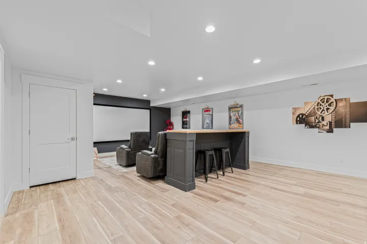 Spacious entertainment area featuring wood-finish flooring, recessed lighting, and a built-in bar with a wooden countertop