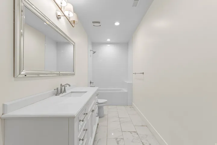 White vanity with a single basin, brushed nickel faucet, and a large framed mirror with sconce lighting