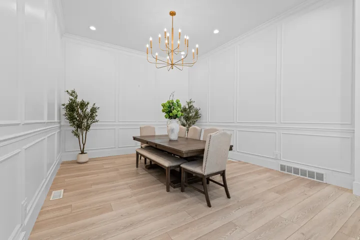 Dining space featuring extensive wall paneling, a contemporary gold-finish chandelier, recessed ceiling lighting, and light wood-finish flooring