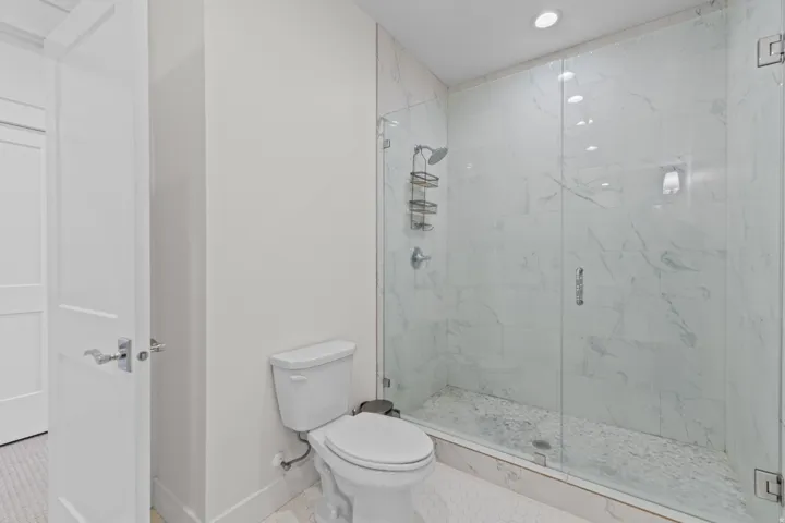 Walk-in shower with clear glass enclosure, white marbled tile surround, and pebble stone floor
