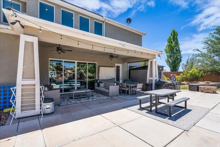 Expansive concrete patio featuring a covered outdoor living area, large sliding glass doors, multiple ceiling fans, and string lighting