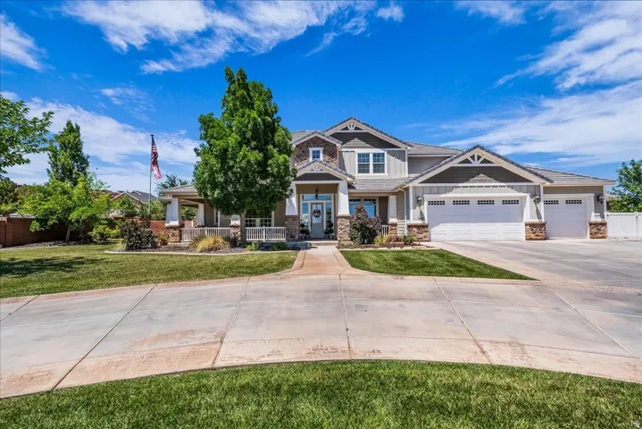 Expansive residence featuring a multi-gable roofline, stone and siding exterior, large front porch with white railings, and a wide paved driveway
