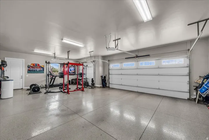 Spacious garage featuring a finished epoxy floor, multiple fluorescent light fixtures, two overhead garage doors with window panels, and a white access door