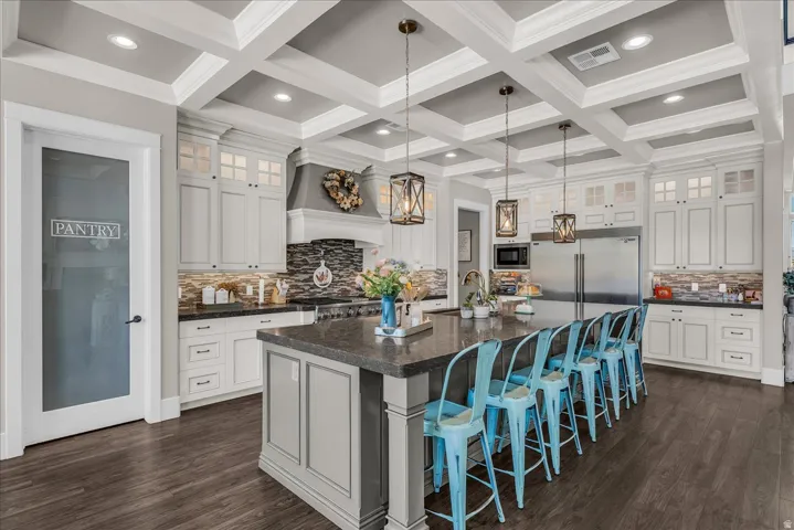 Kitchen featuring coffered ceilings, wood-finish flooring, a large central island with seating, extensive cabinetry, and stainless steel appliances