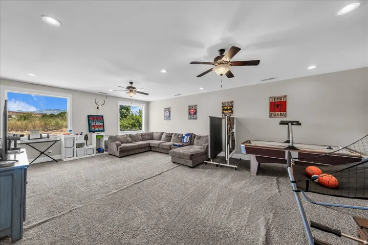 Spacious recreation room featuring light gray carpeting, multiple recessed lights, and two ceiling fans