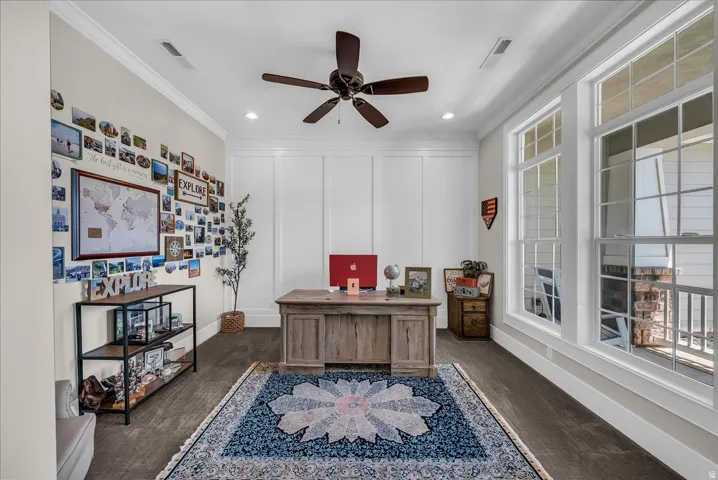 Spacious room featuring rich wood-finish flooring, white paneled wall accents, and abundant natural light from multiple large windows