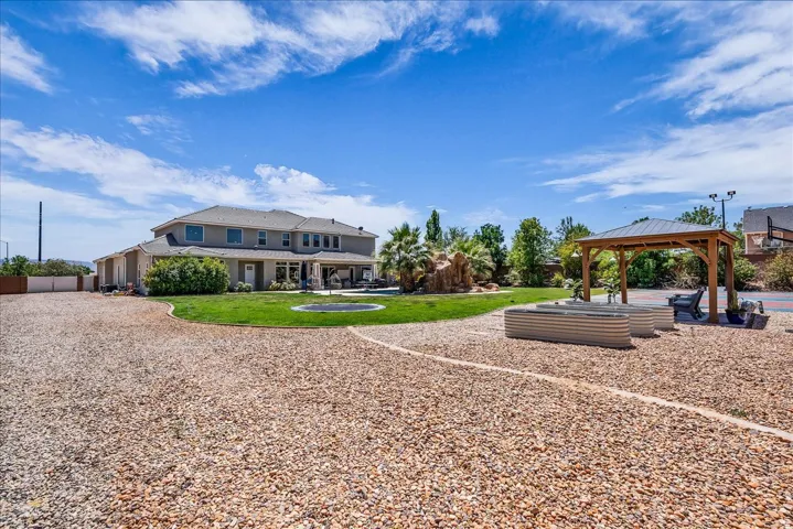 Expansive gravel hardscaping with a detached gazebo, raised garden beds, and a two-story home with a covered patio