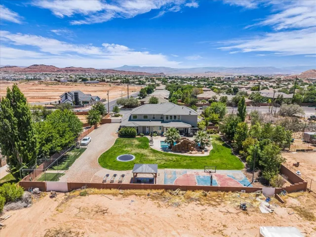 Aerial property overview featuring a substantial residence with a gravel driveway, a manicured lawn, a built-in outdoor basketball court, and a poolside rock grotto with water features