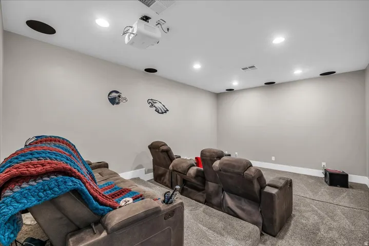Dedicated media room featuring a ceiling-mounted projector, recessed lighting, integrated ceiling speakers, and plush carpeting