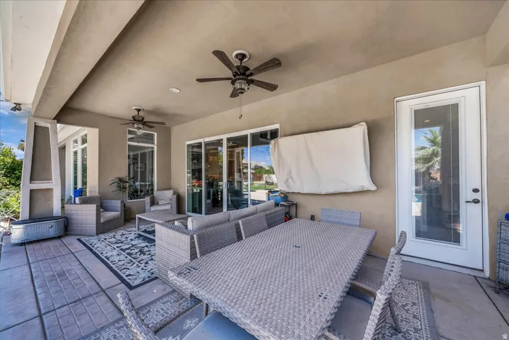Covered outdoor patio featuring a textured concrete floor, multiple ceiling fans, and an exterior door with a full-light panel