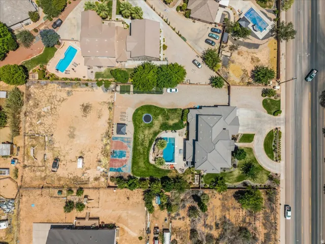 Expansive property featuring a large residence with a multi-gabled roofline, a private swimming pool, a dedicated sports court, a circular drive, and a manicured lawn area
