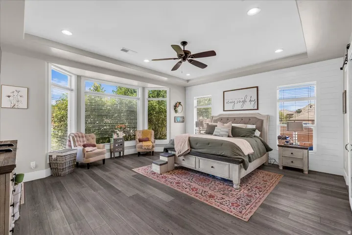 Spacious bedroom featuring a bay window with multiple panes, wood-finish flooring, a ceiling fan, recessed lighting, and a shiplap accent wall