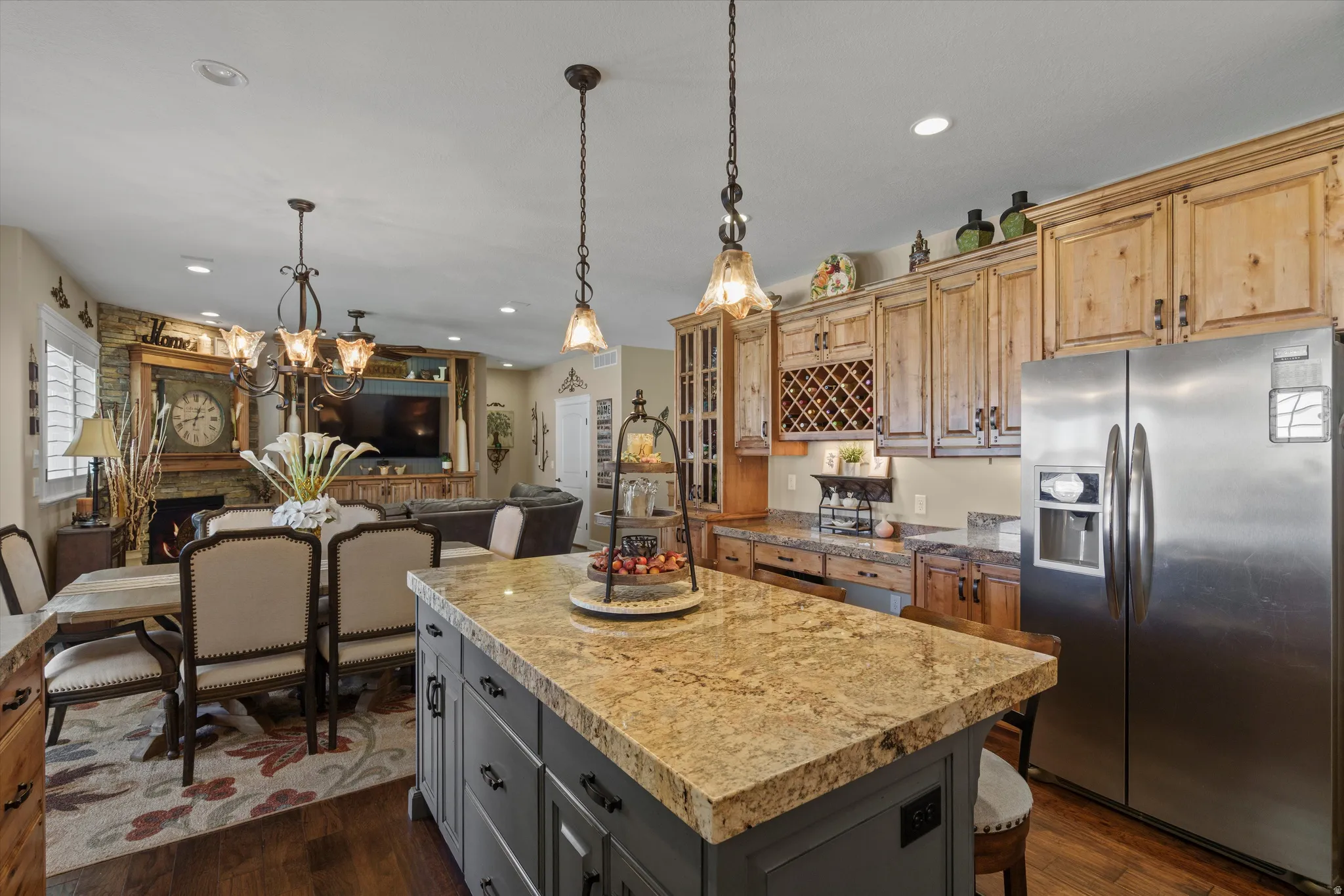 Spacious kitchen featuring a large island with a stone-finish countertop, stainless steel refrigerator, wood-finish cabinetry, and built-in wine storage