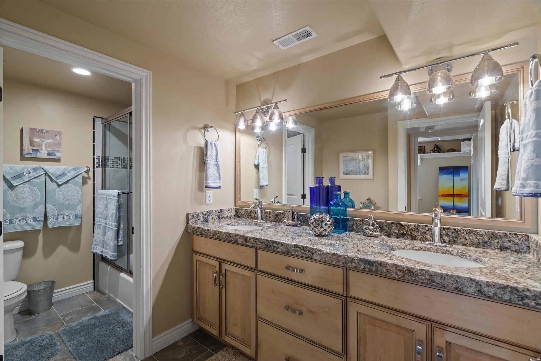 Bathroom featuring a dual-sink vanity with a light-toned countertop, wood-finish cabinetry, and a large wall-mounted mirror