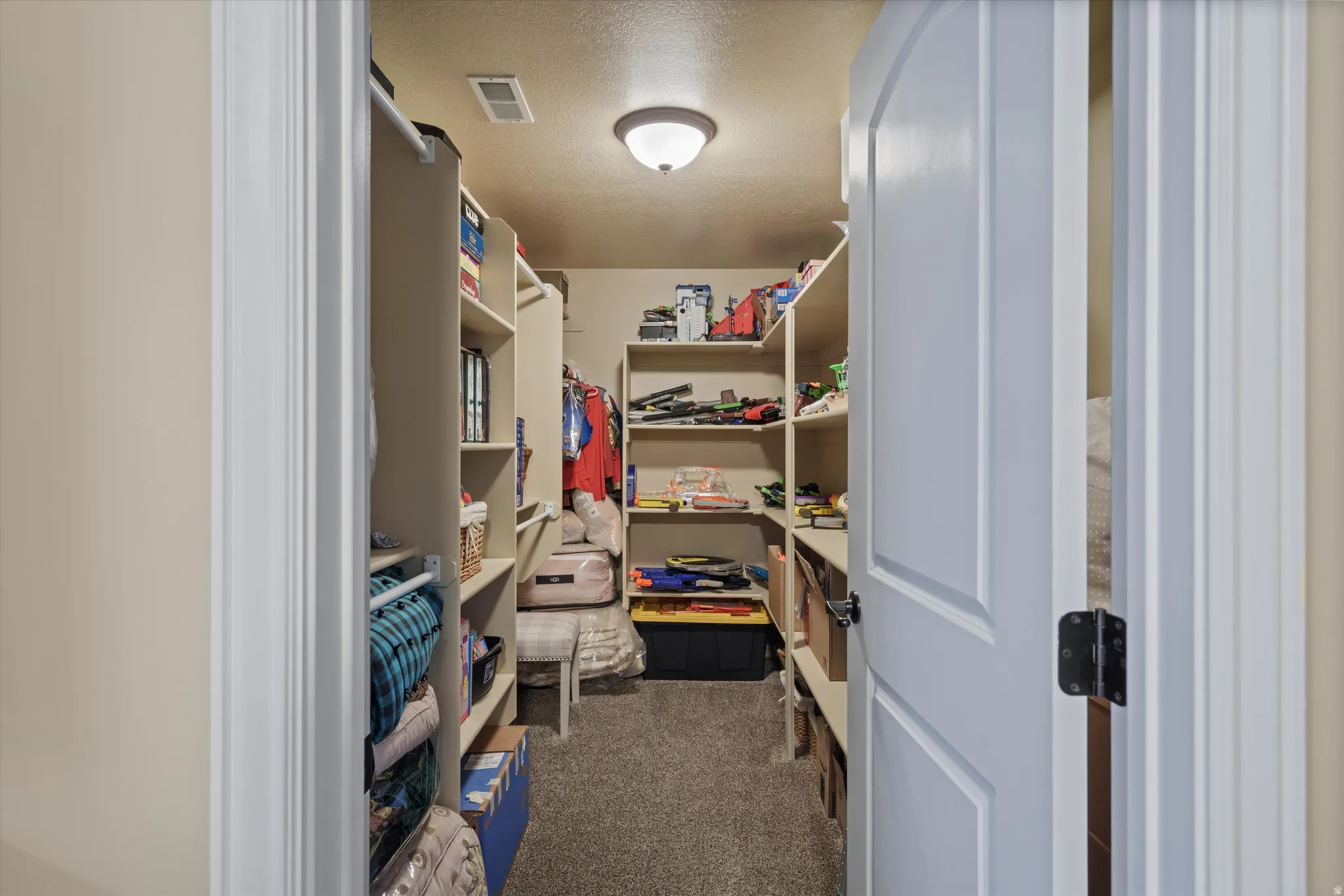 Walk-in closet featuring extensive built-in shelving, hanging rods, recessed ceiling light fixture, and carpet flooring