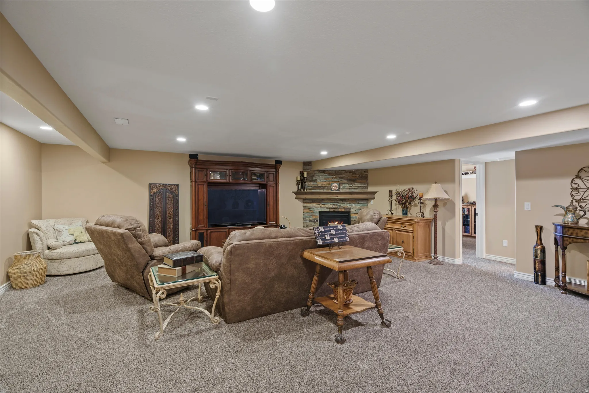 Carpeted recreation room featuring a stone-front fireplace with a wood mantle, recessed lighting, a built-in entertainment center, and neutral paint tones