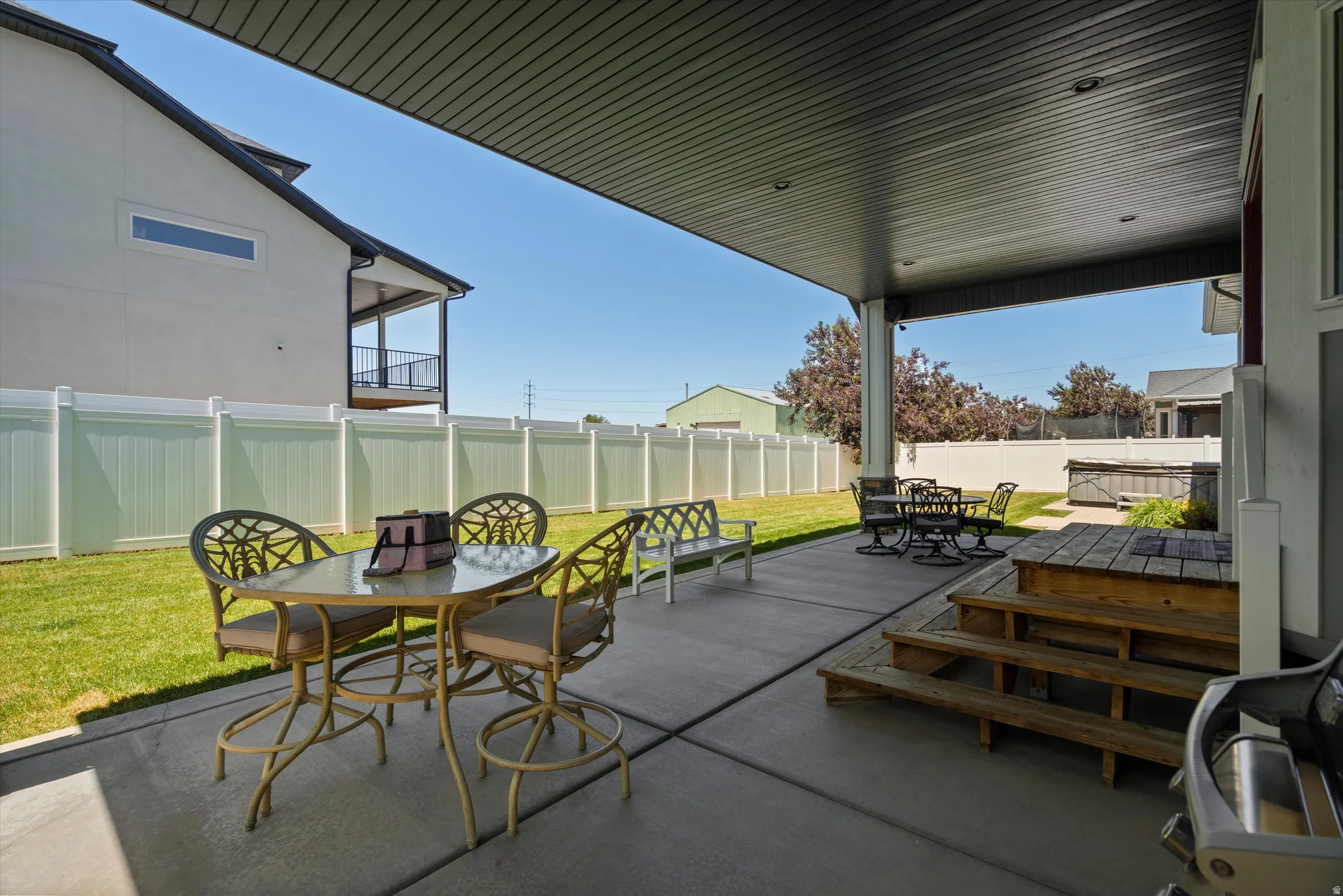 Covered patio featuring concrete flooring, a white vinyl fence, and a manicured lawn