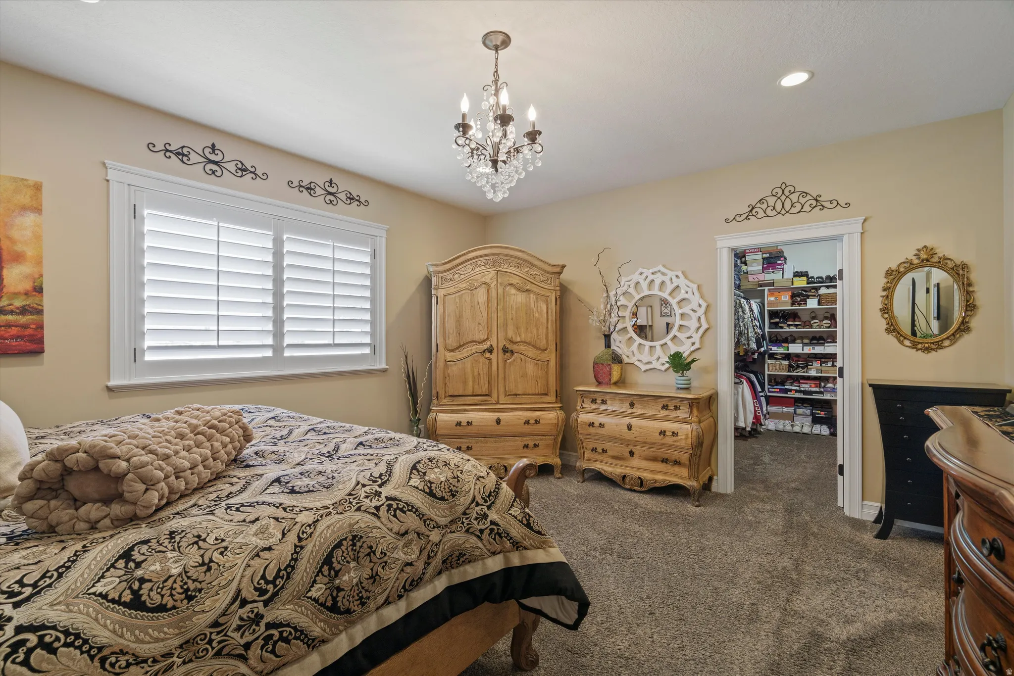 Plush carpeted bedroom featuring a crystal chandelier, recessed lighting, and a window with white louvered shutters
