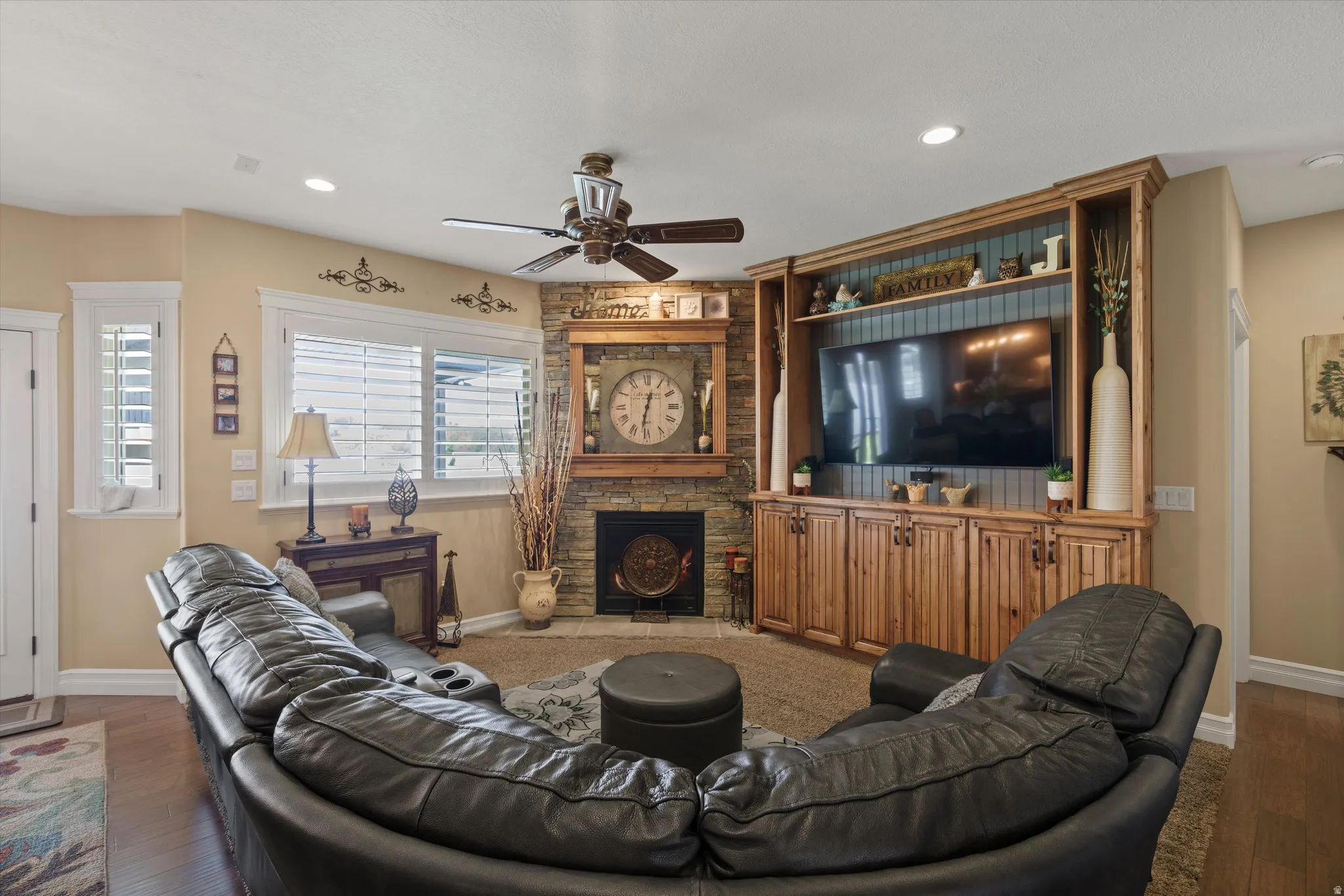 Living area featuring a stone-clad fireplace, wood-finish mantel, and a built-in entertainment center with open shelving and cabinet storage