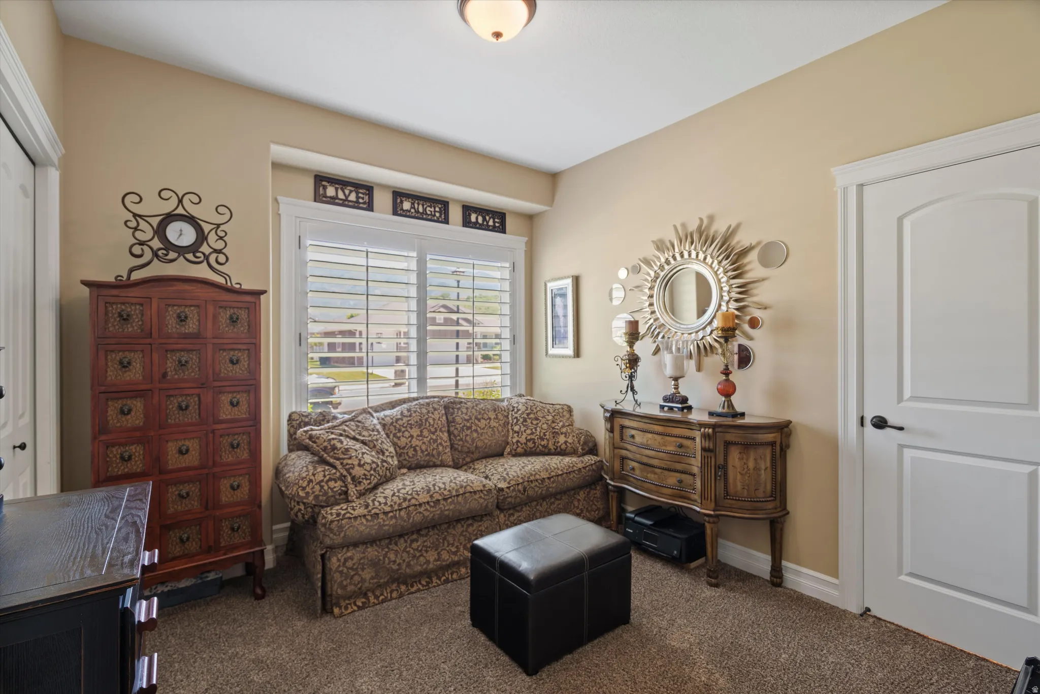 Carpeted room featuring a window with white plantation shutters, a white paneled door with black hardware, and light beige wall paint