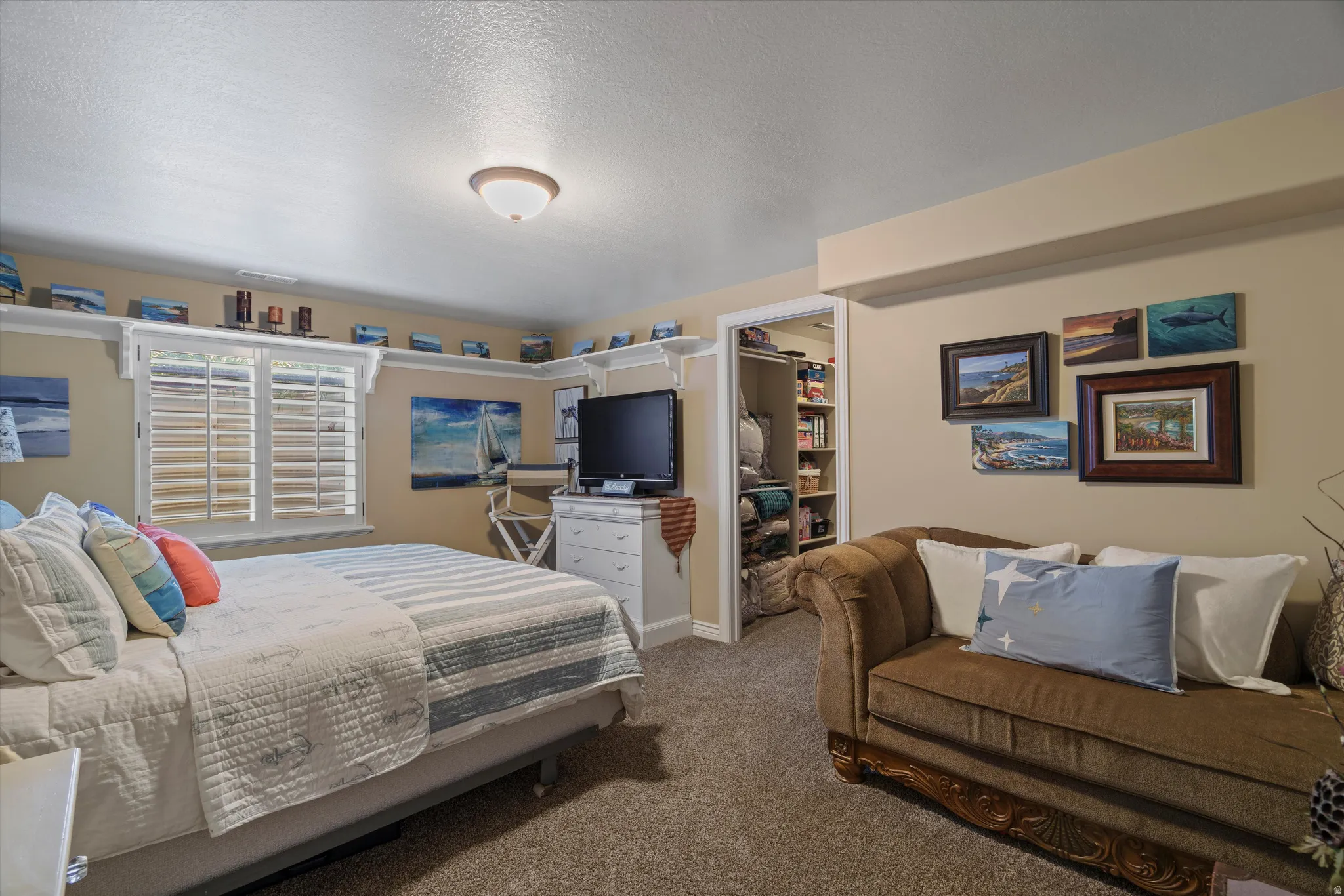 Carpeted room featuring a window with white louvered shutters, a built-in shelf system spanning multiple walls, a recessed ceiling light fixture, and an open doorway revealing a closet with shelving