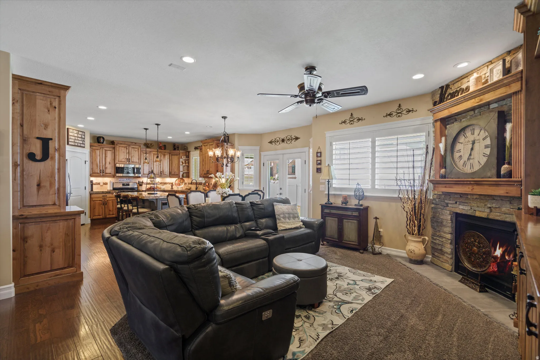 Open-concept living space featuring wood-finish flooring, a stone-faced fireplace with a wood mantle, recessed lighting, and a ceiling fan