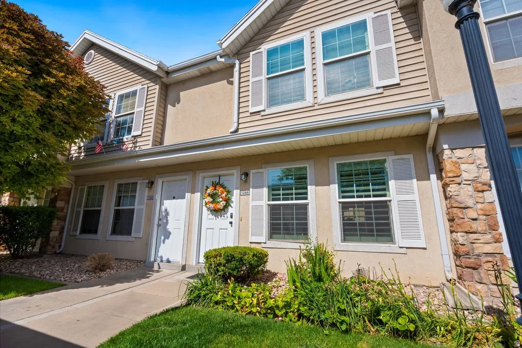 Multi-level townhome exterior featuring beige siding, stone accents, and white window shutters