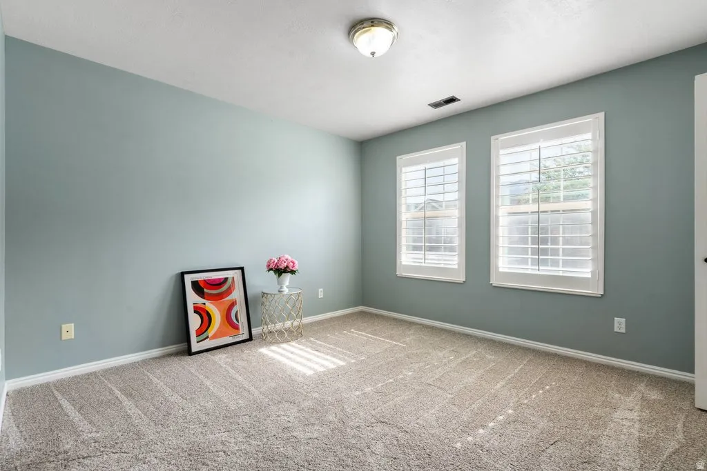 Room featuring two windows with white plantation shutters, neutral-toned carpet flooring, light blue wall paint, white baseboards, and a semi-flush mount ceiling light fixture