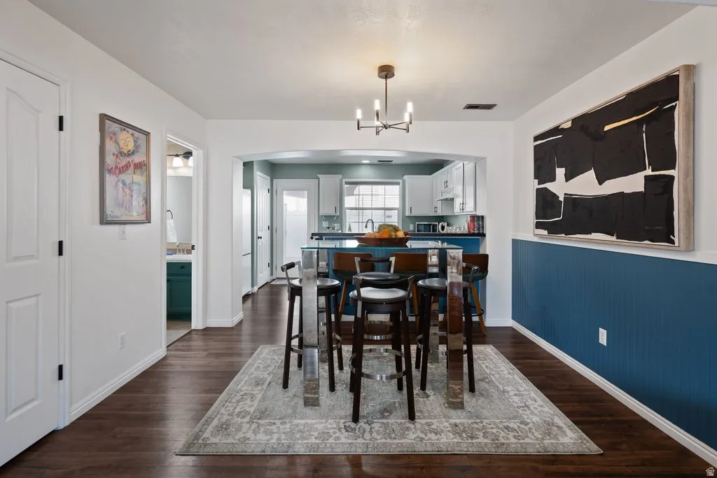 Open-concept dining area featuring dark wood-finish flooring, a contemporary chandelier, and a decorative wall panel accent