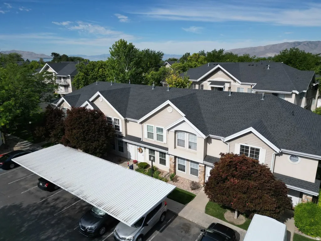 Multi-level townhome exterior featuring light-toned siding, dark shingle roofing, and a covered parking structure
