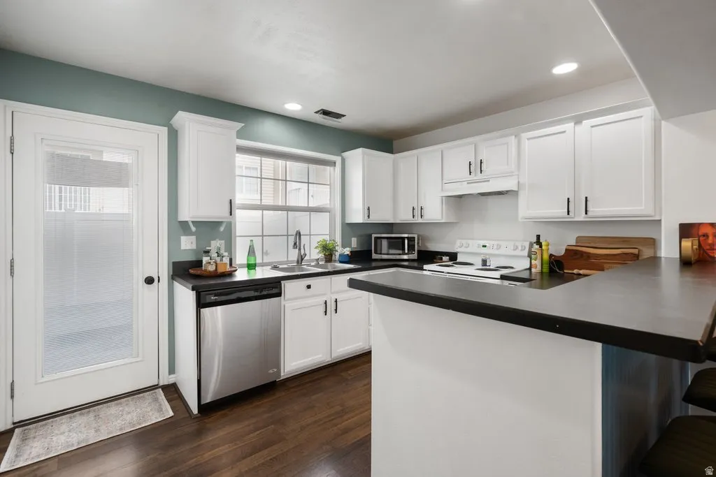 Kitchen featuring white cabinetry, dark countertops, wood-finish flooring, and stainless steel appliances