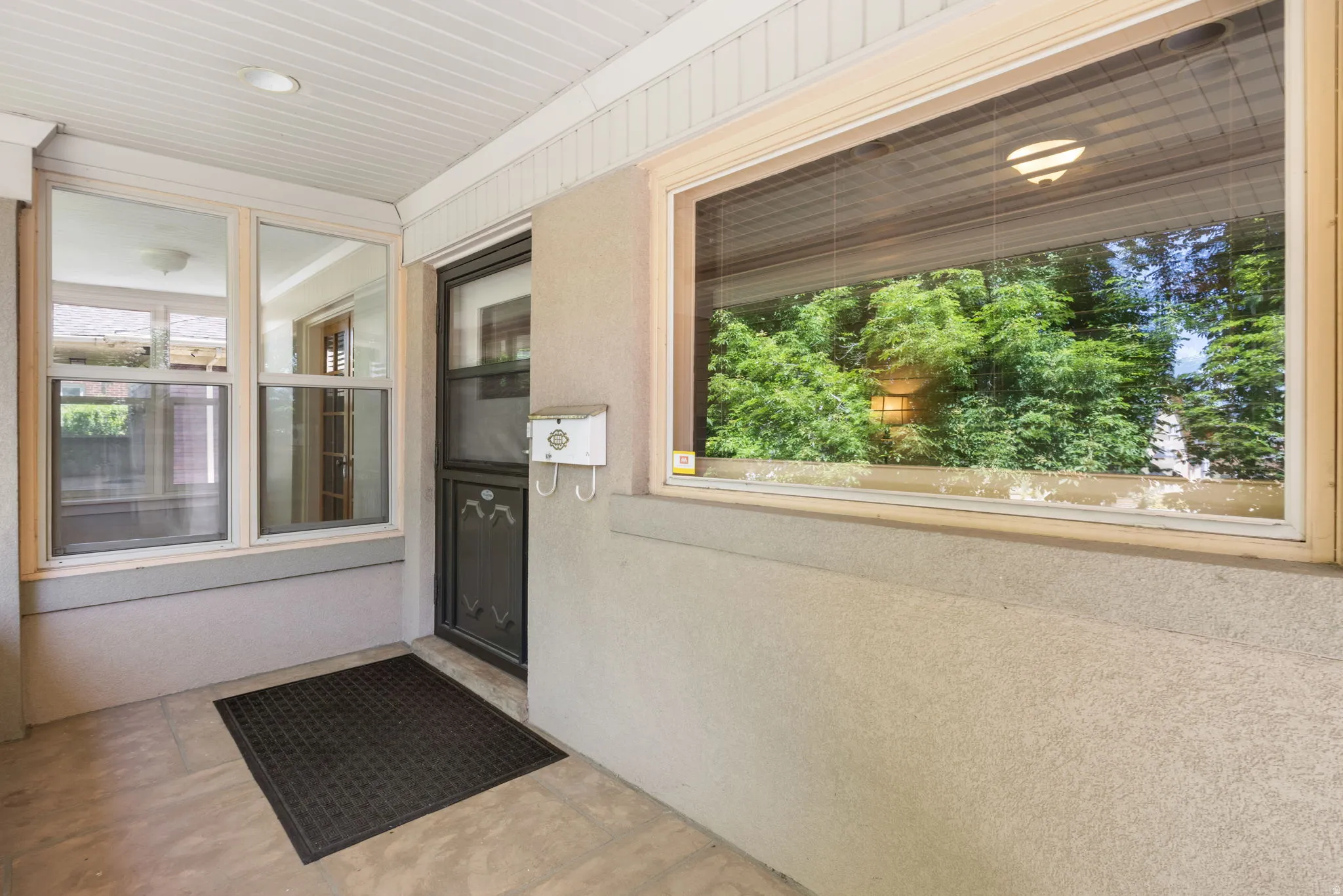 Covered porch entry featuring a dark-framed screen door, a recessed ceiling light, and a horizontal window with a green outdoor backdrop