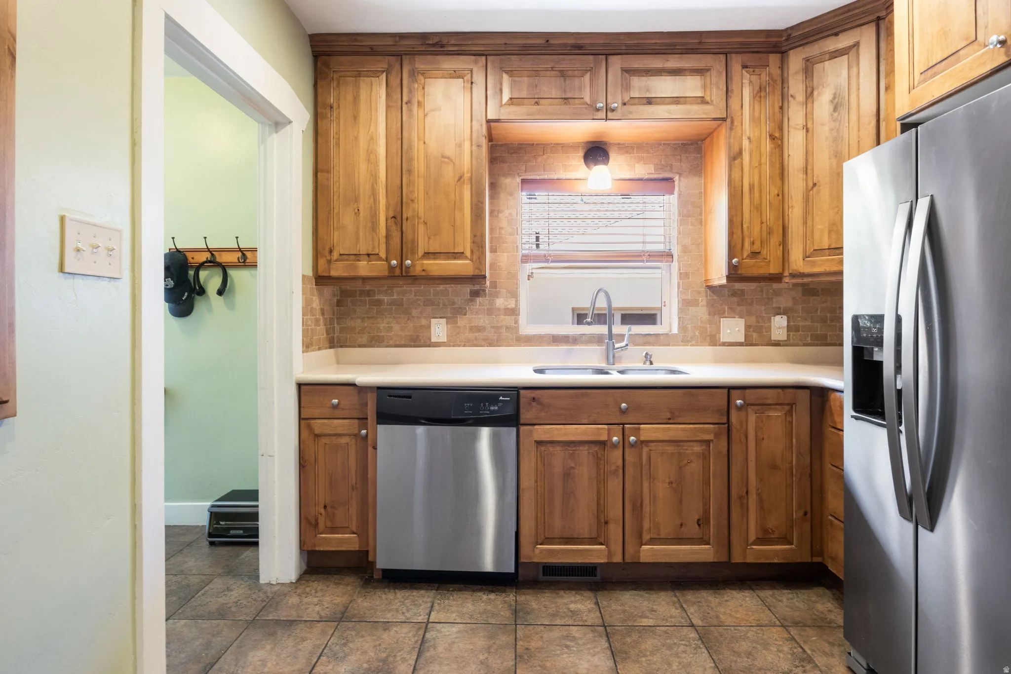 Kitchen featuring wood cabinetry, stainless steel appliances, a double basin sink, light-toned countertops, and a tiled backsplash