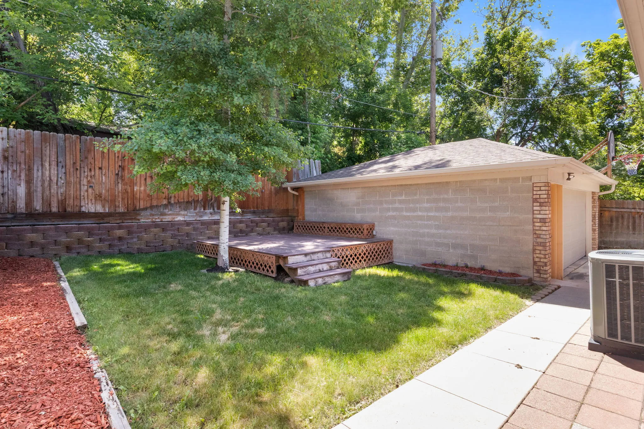 Spacious backyard featuring a multi-level wooden deck, mature tree, and a detached garage with a brick facade