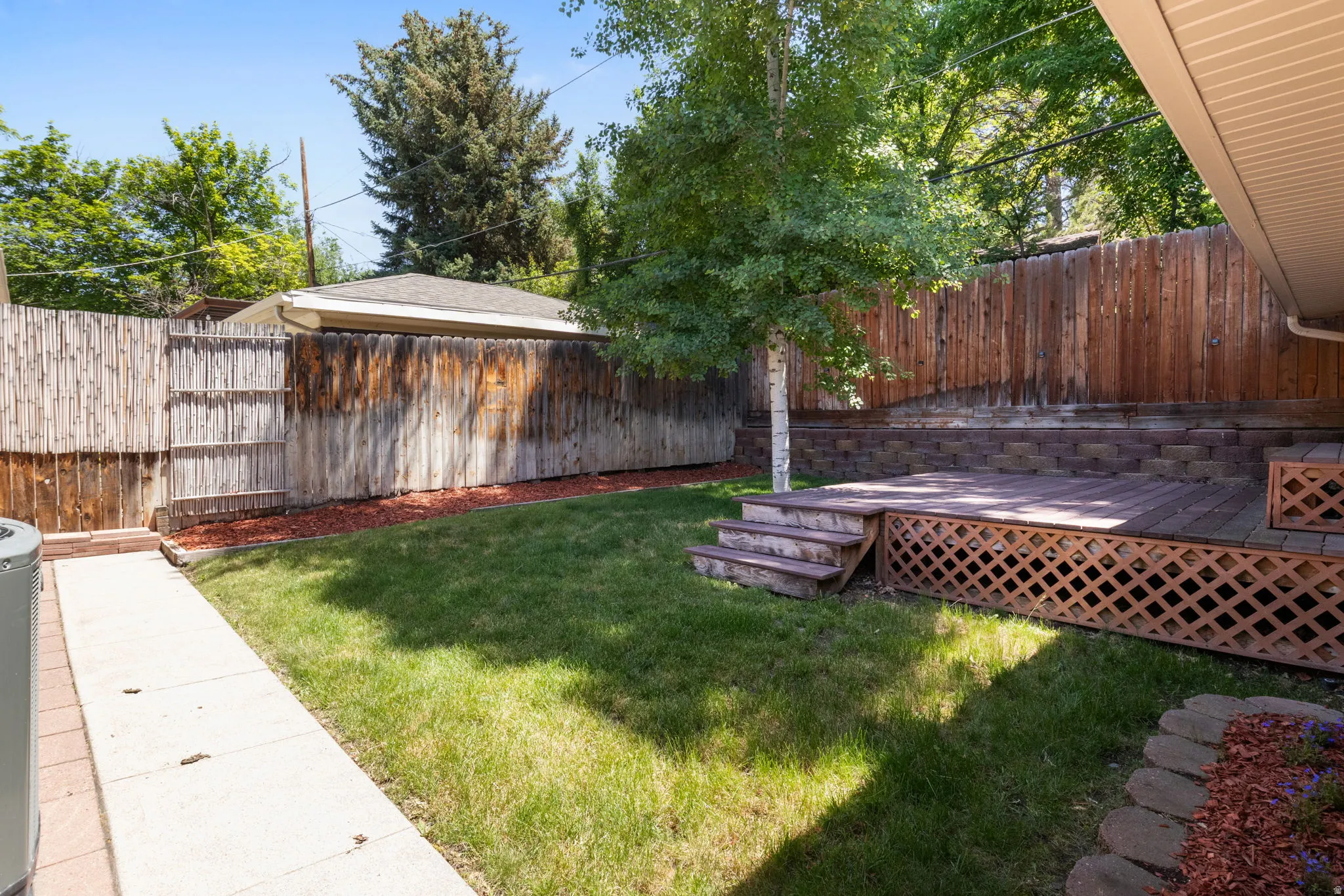Expansive backyard featuring a tiered wooden deck with lattice skirting, a manicured lawn, and mature trees