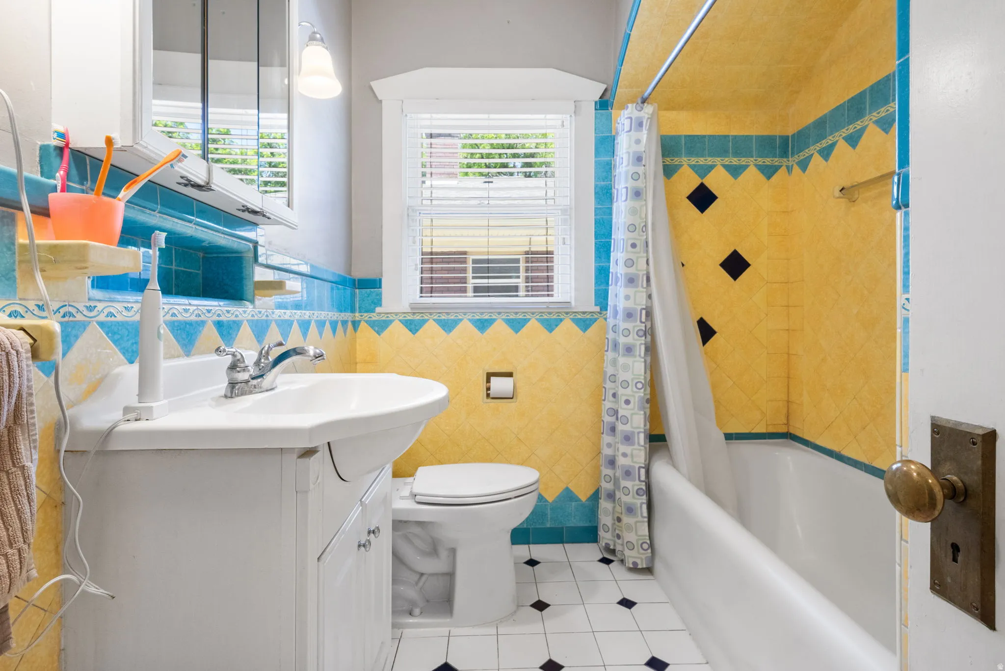 Bathroom featuring pedestal sink, white toilet, and a combination tub and shower with yellow and blue wall tile