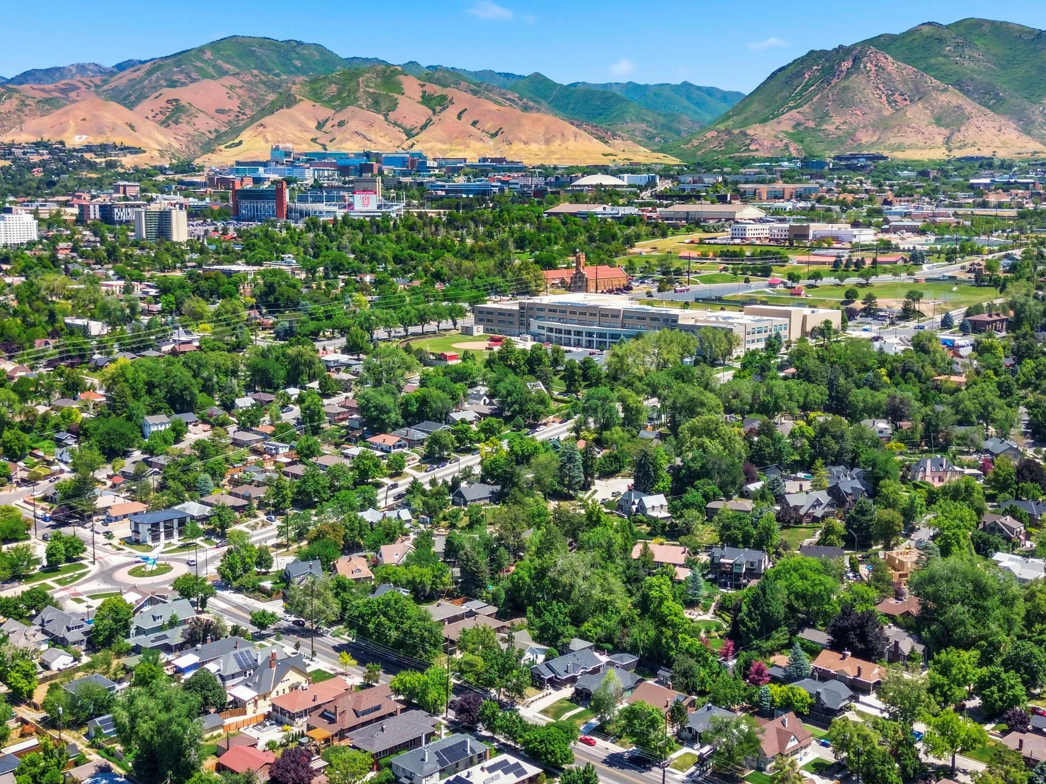 Expansive aerial landscape highlighting a residential neighborhood with established trees, framed by distant mountains