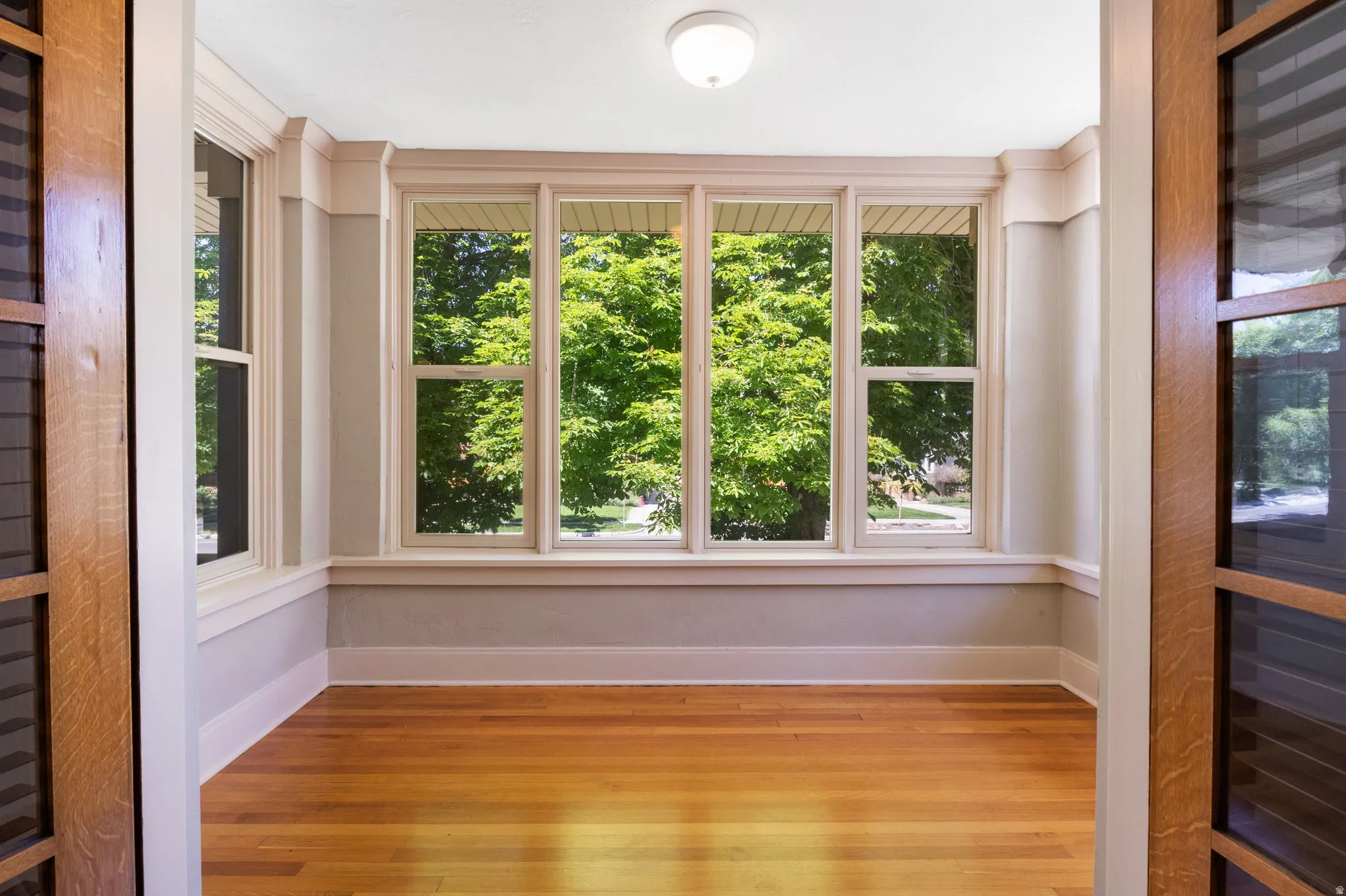 Bright room featuring a multi-pane window array, wood-finish flooring, white baseboards, and a flush-mount ceiling light fixture