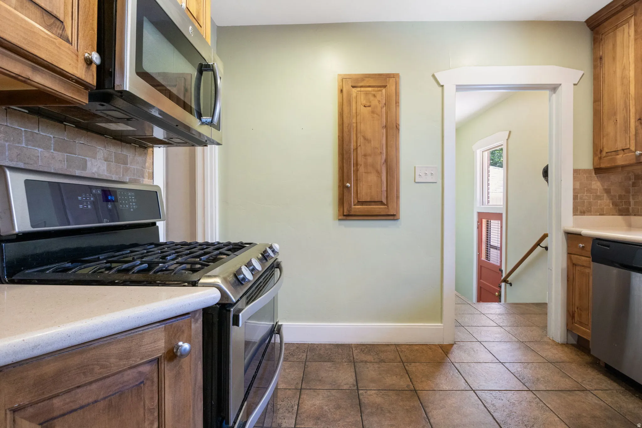 Kitchen featuring stainless steel appliances, tiled floors, wood-finish cabinetry, light countertops, and a subway tile backsplash