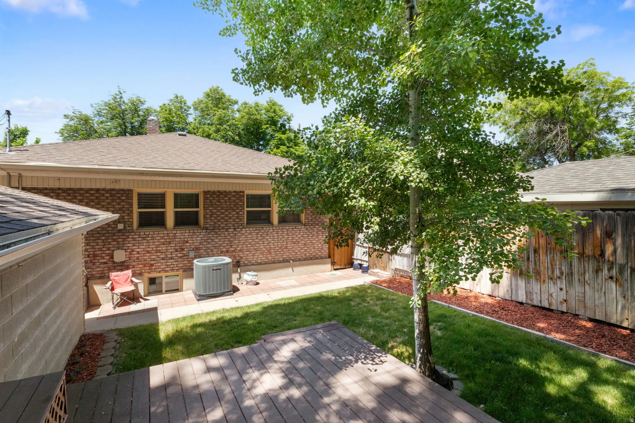 Expansive backyard featuring a wood-finish deck, a manicured lawn, and a mature tree