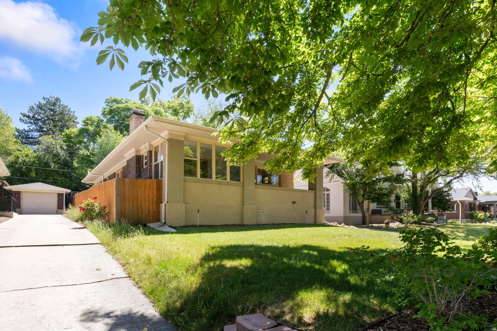 Mature tree canopies shade a verdant lawn, framing a stucco exterior with a prominent window bank