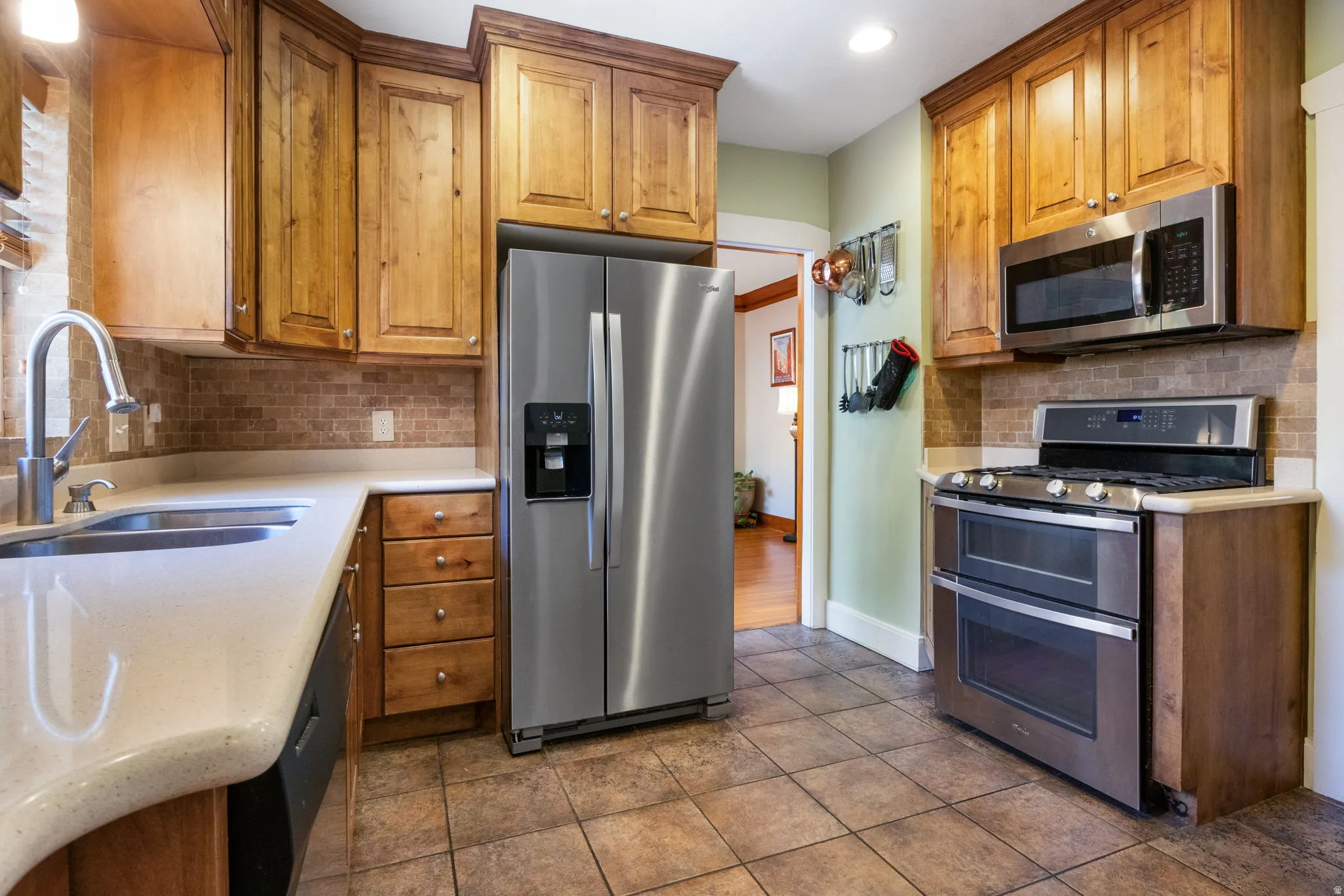 Kitchen featuring wood cabinetry, stainless steel appliances, a double oven range, tile flooring, and a stone-finish countertop with an undermount sink