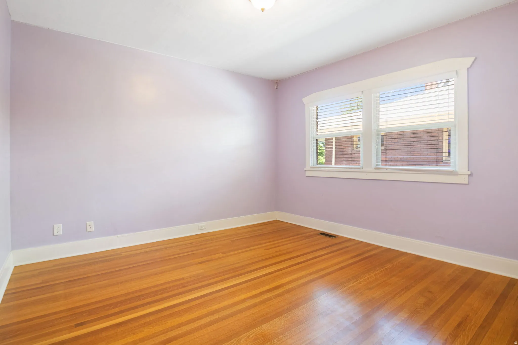 Room featuring wood-finish flooring, light purple wall paint, white baseboards, and white window trim