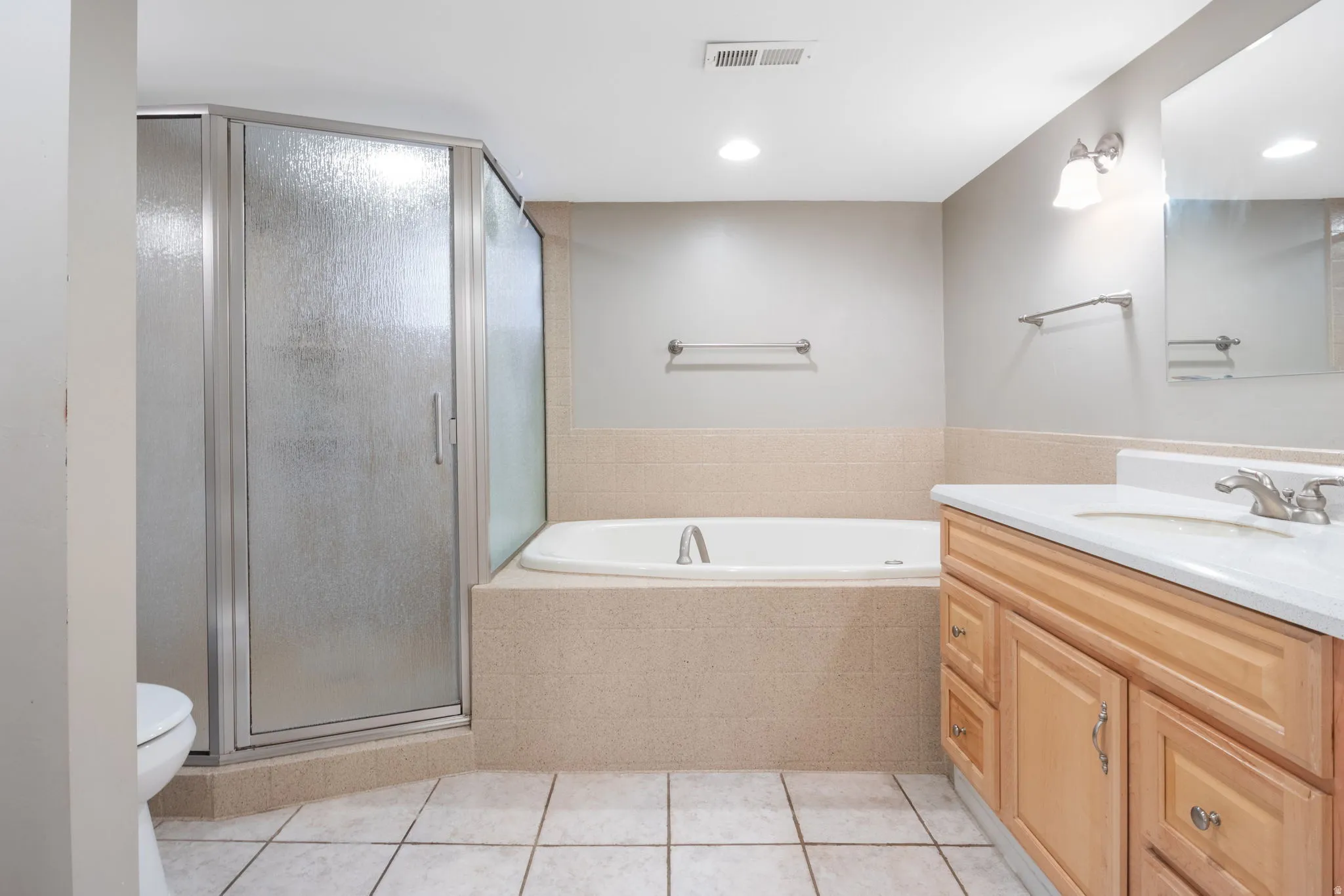 Bathroom featuring a glass-enclosed shower, a built-in soaking tub with a tiled surround, a light wood-finish vanity with a white countertop and integrated sink, and white square floor tiles