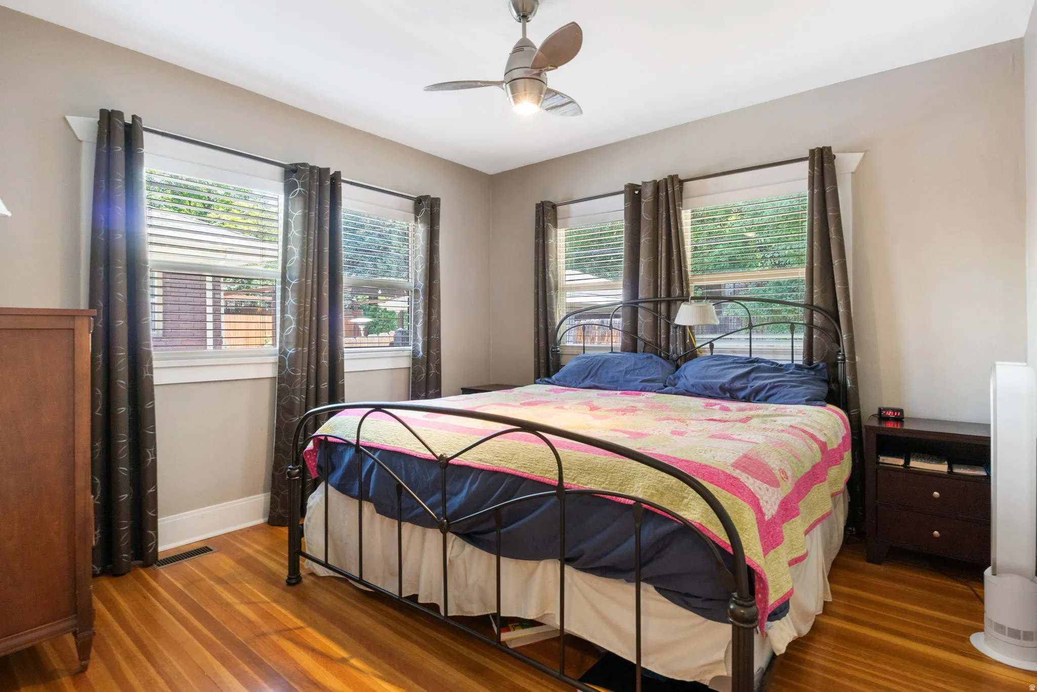 Bedroom featuring two windows with white trim, wood-finish flooring, and a ceiling fan with integrated lighting