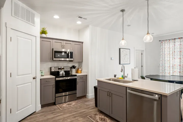 Kitchen featuring wood-finish flooring, two-tone cabinetry, stainless steel appliances, and a central island with a sink