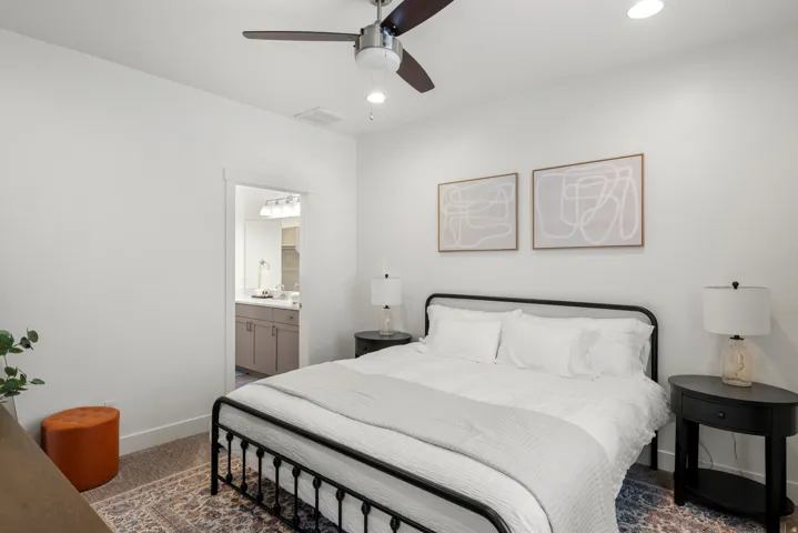 Neutral bedroom featuring a ceiling fan, recessed lighting, and a doorway to a bathroom with a vanity and mirror