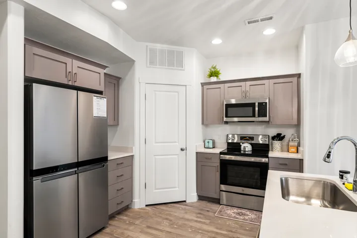 Contemporary kitchen with wood-finish flooring, two-tone cabinetry, stainless steel appliances, recessed lighting, and light countertops
